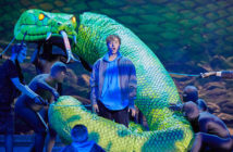 performer surrounded by snake prop operated by other performers