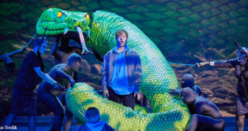 performer surrounded by snake prop operated by other performers